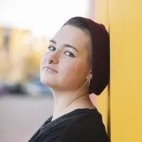 Young person wearing beanie hat standing against a yellow wall