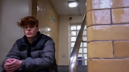 Photograph shows homeless young person sat on a staircase.