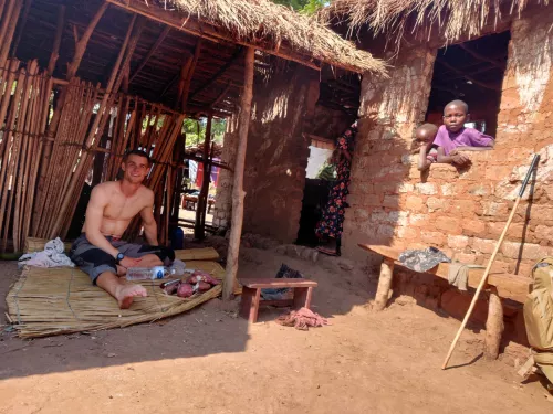 Photograph of Ben Harris outside outside on a mat and two children can be seen next door looking through the window at the camera. 