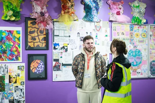 Dean McCullough stands by a display of work and chats with staff at Manchester Enterprise Academy 