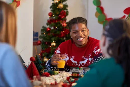 A young person wearing a festive red jumper sits at the dinner table enjoying a Christmas dinner