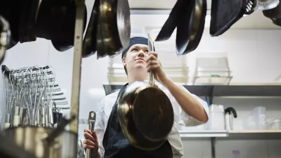 Young person in a professional kitchen hanging up pans