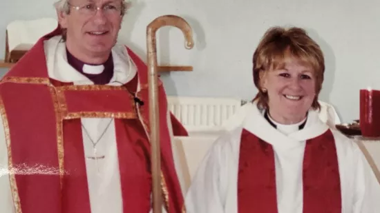 Freda stands and smiles wearing a Christian robe in a Church