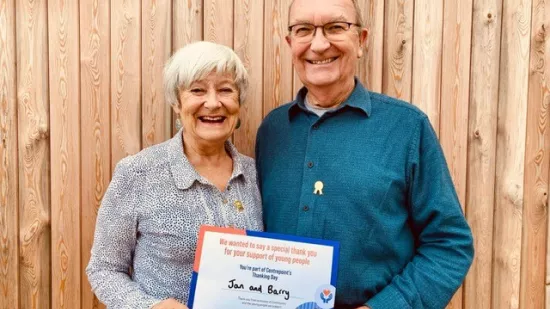 Jan and Barry hold their Thanking Day certificate outside the garden shed where they held their Sleep Out fundraiser.