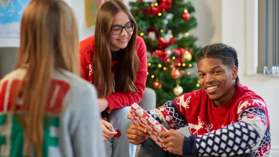 A group of young people sit around a Christmas tree and exchange gifts