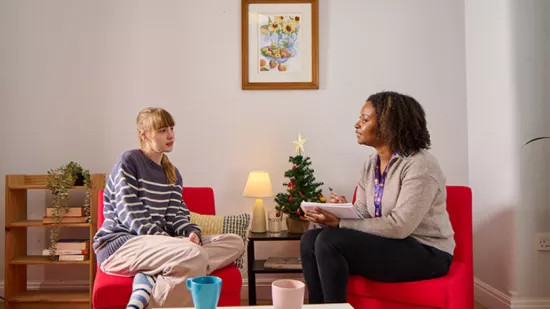 A young person and a key worker sat on chairs facing each other having a conversation, with a Christmas tree in the background.