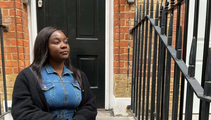 Picture shows young person sat on some steps outside a black front door.