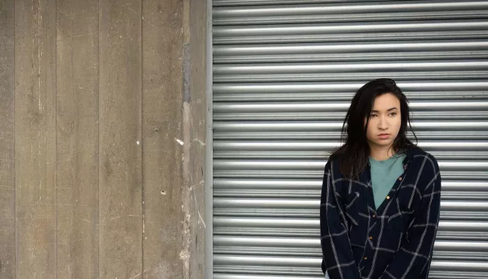 Homeless young person standing against a metal shutter.