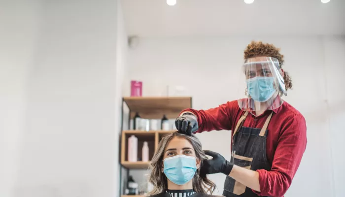 Young person wearing PPE, cuts a customer's hair