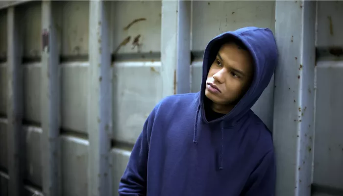 Young mixed race person in blue hoodie leaning against concrete wall