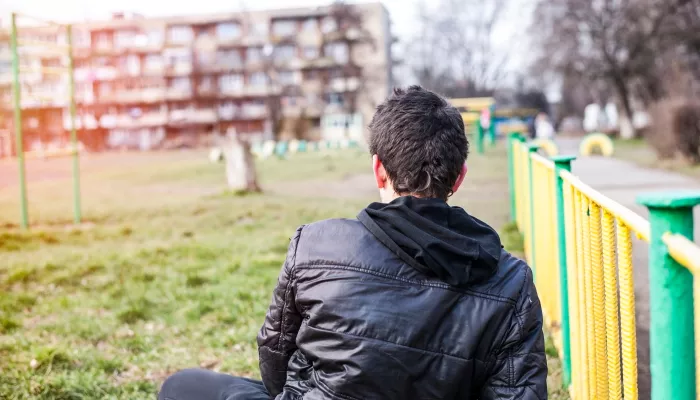 person sitting on grass with back to the camera looking towards a block of flats