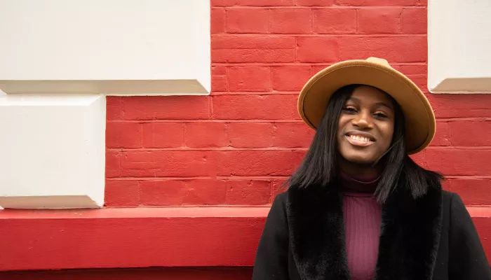 Young person wearing a wide-brimmed hat in front of red brick wall