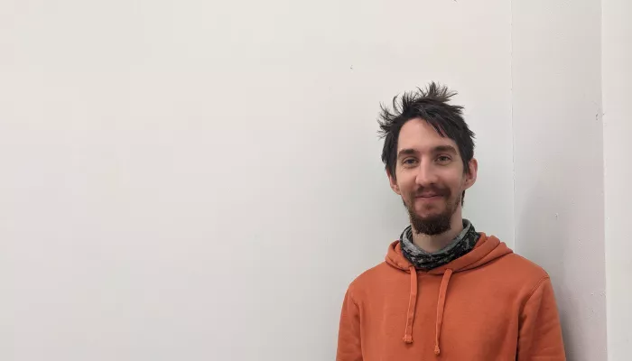 Young person with dark hair wearing an orange hoody against a white background