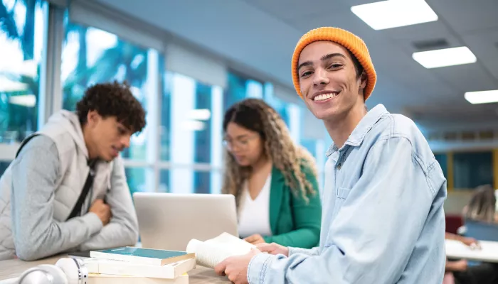 Young person wearing orange beanie sitting at a desk and smiling