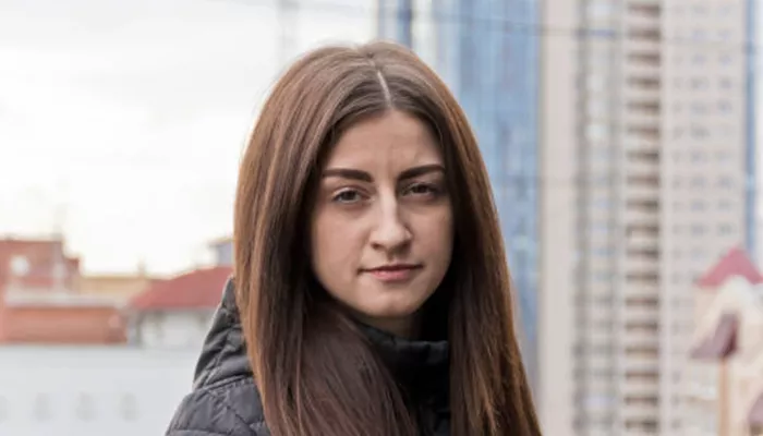 Young person standing in front of river and tall buildings