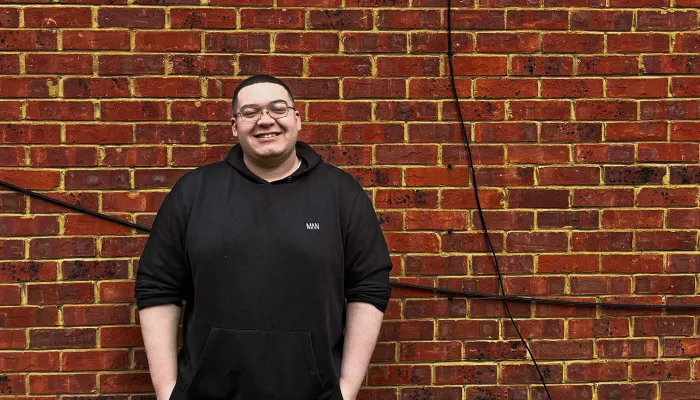 Young person in black hoodie standing against a brick wall.