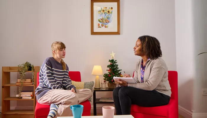 One young person and one key worker sat facing each other on chairs, having a conversation. With a Christmas tree in the background.