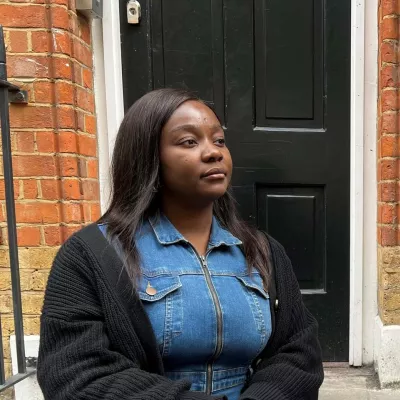 Picture shows young person sat on some steps outside a black front door.