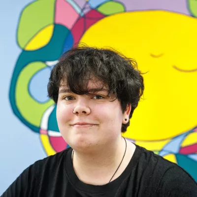 Photograph of young person against a brightly coloured mural.