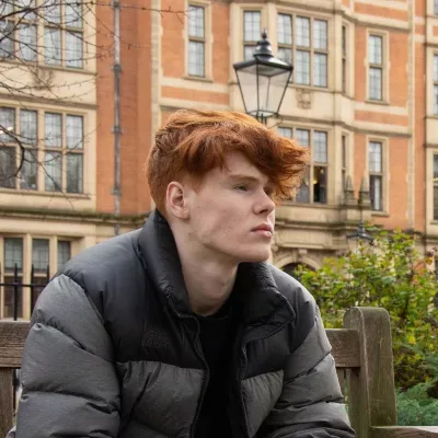 Young person sat outside on a bench looking off camera.