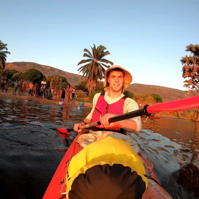 Photograph of Ben Harris, fundraiser, in a kayak on a lake. Ben is wearing a hat and trees can be seen in the background