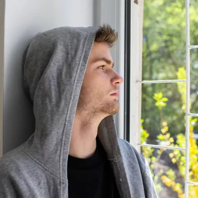 Young person wearing grey hoodie gazes out of a window