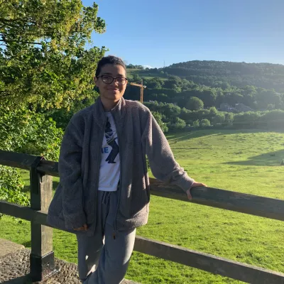 Young person standing my a gate leading to fields in the sunshine