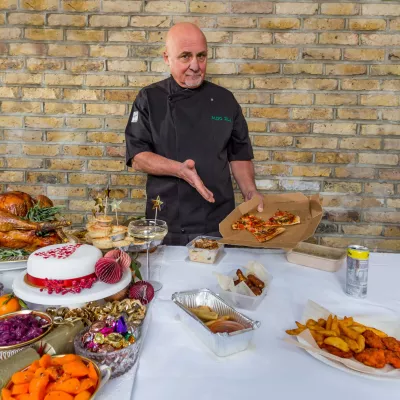 Chef Aldo Zilli presents a beautiful spread of food, including turkey, pigs in blankets, cake, sweets, carrots, mince pies, and contrasts with takeaways to show the difference for homeless people at Christmas.