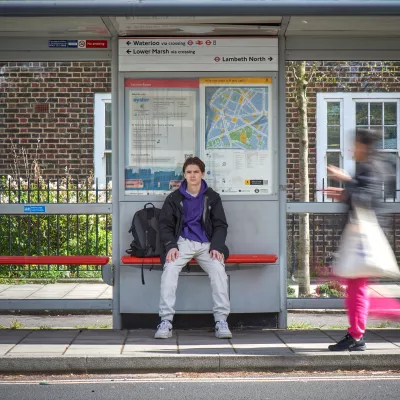 Young person at bus stop with rucksack.