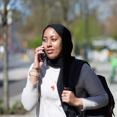 Young person, outside, wearing a rucksack and with a mobile phone to their ear.