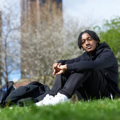 Young person outside sitting on the grass with their rucksack