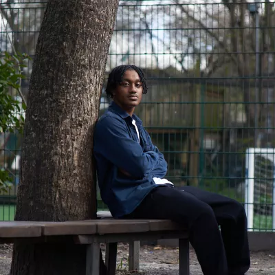 Young person leans against a tree with their arms crossed