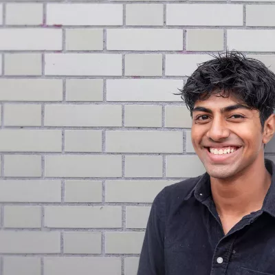 smiling young person standing against a grey brick wall