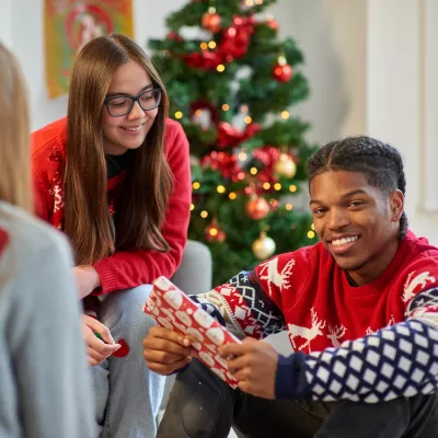 A group of young people sit around a Christmas tree and exchange gifts