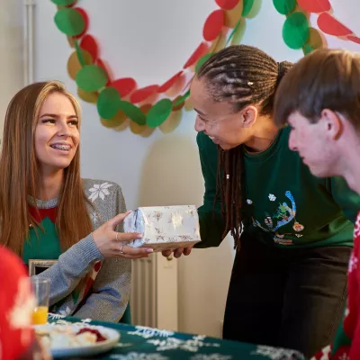 A group of young people receive gifts for Christmas, smiling next to the tree